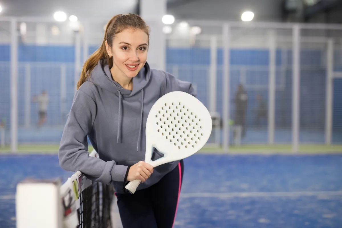 Gadis Amerika memakai hoodie jaket sambil menggenggam raket padel warna putih