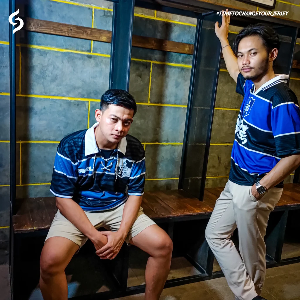 Foto dua pria mengenakan jersi retro berwarna biru garis hitam buatan Street Jersey. Lokasi di dalam ruang ganti pemain.