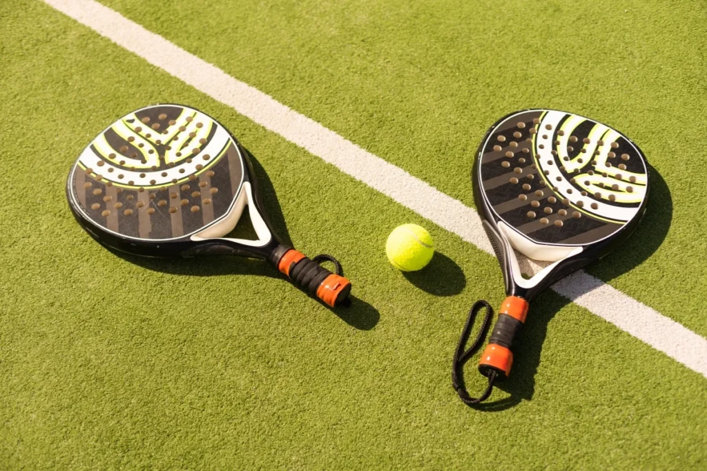 Foto dua raket padel dan bola tenis di atas lapangan hijau