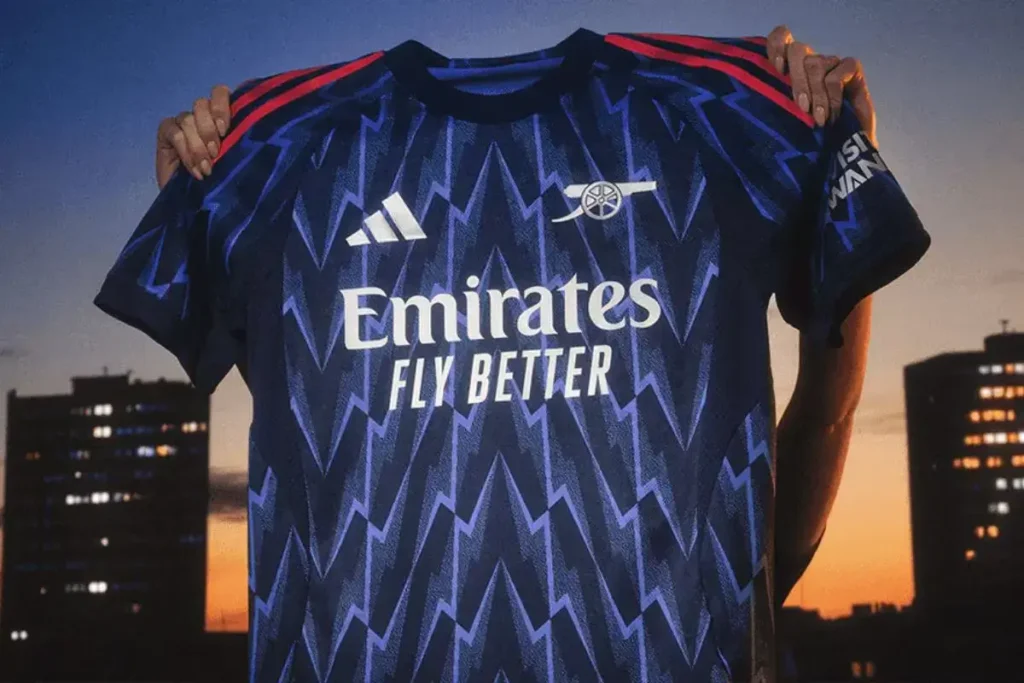 Pria menggenggam jersey Arsenal away 2025-26